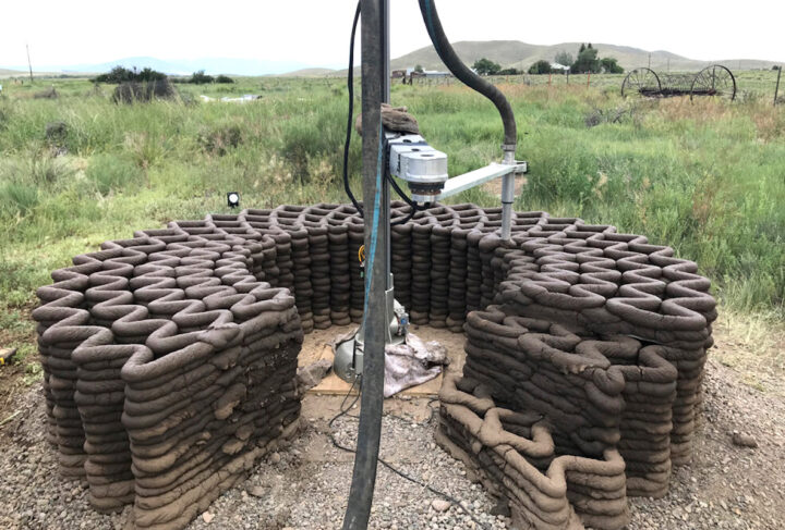 Hose extruding adobe mud in a zig-zag wall pattern in a field
